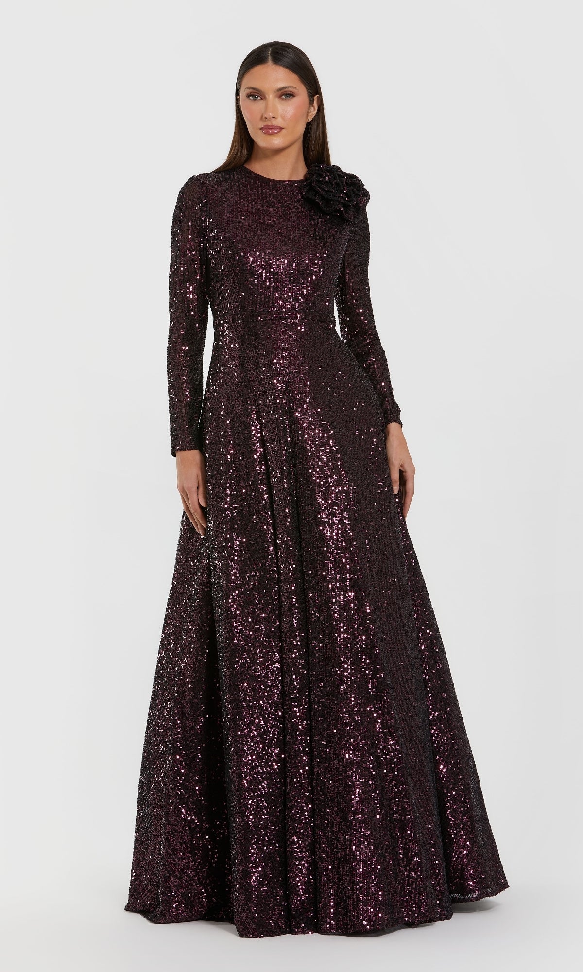 A woman poses against a white background in the Mac Duggal 56178 Amethyst Sequin Formal Dress, featuring a floor-length silhouette, long sleeves, and a floral-embellished shoulder—an elegant mother of the bride choice.
